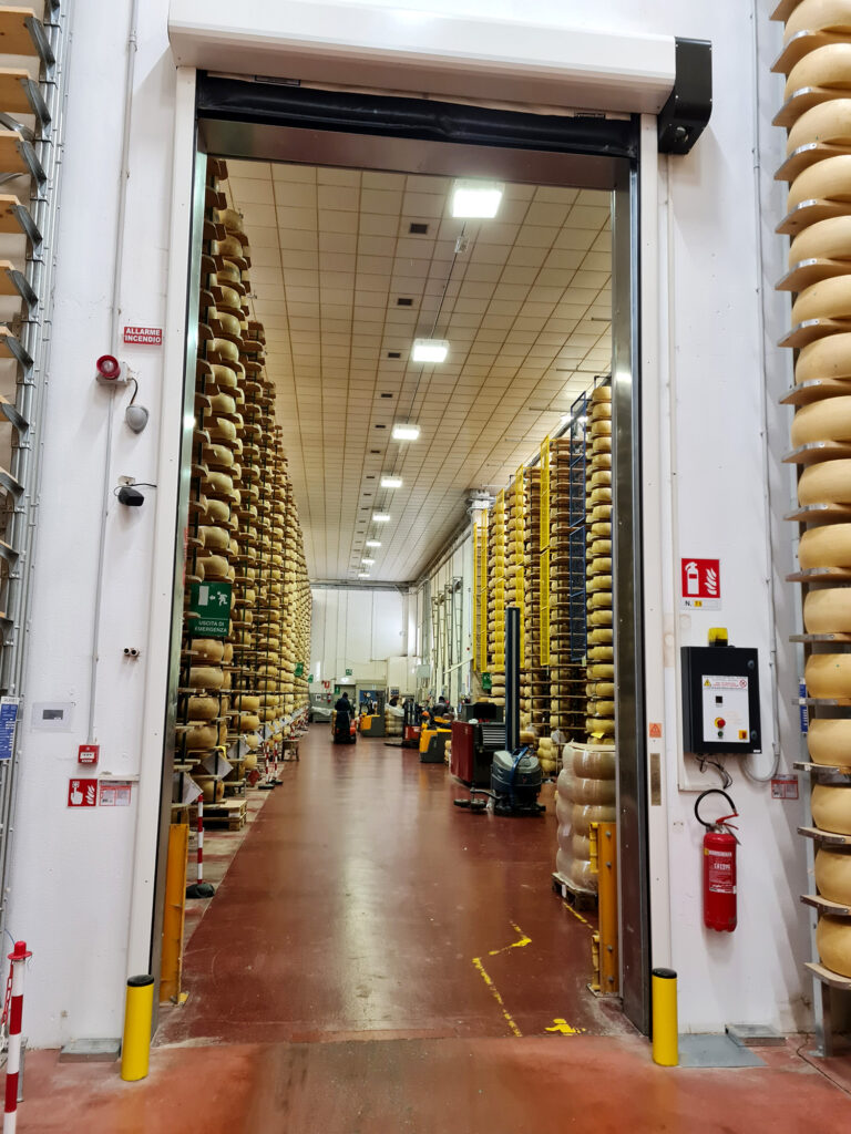 Accesso al magazzino di stagionatura Agriform Parmareggio con porta rapida e scaffalature autoportanti cariche di forme di formaggio.